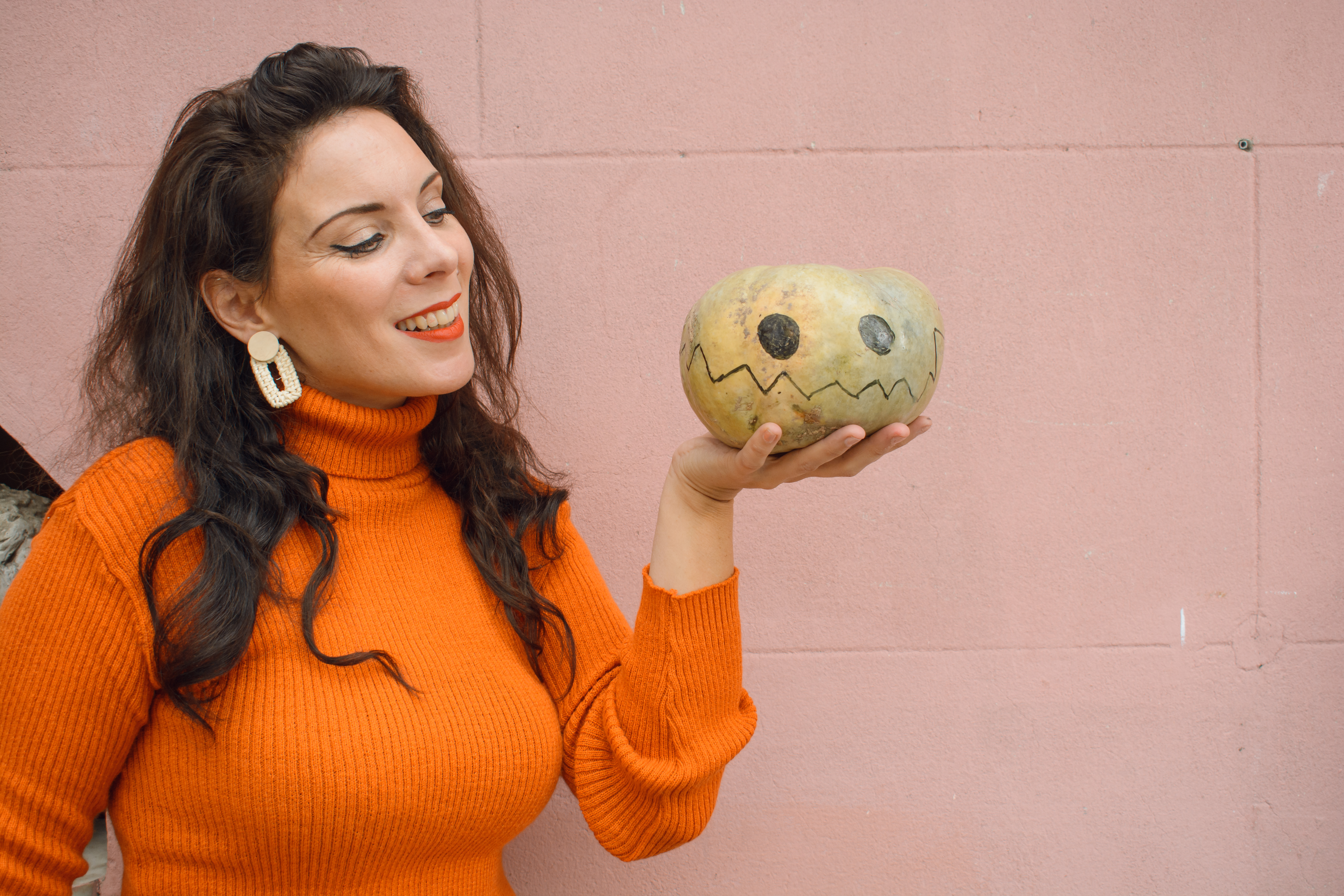 caucasian woman holding halloween pumpkin with her hand standing with pink wall in background